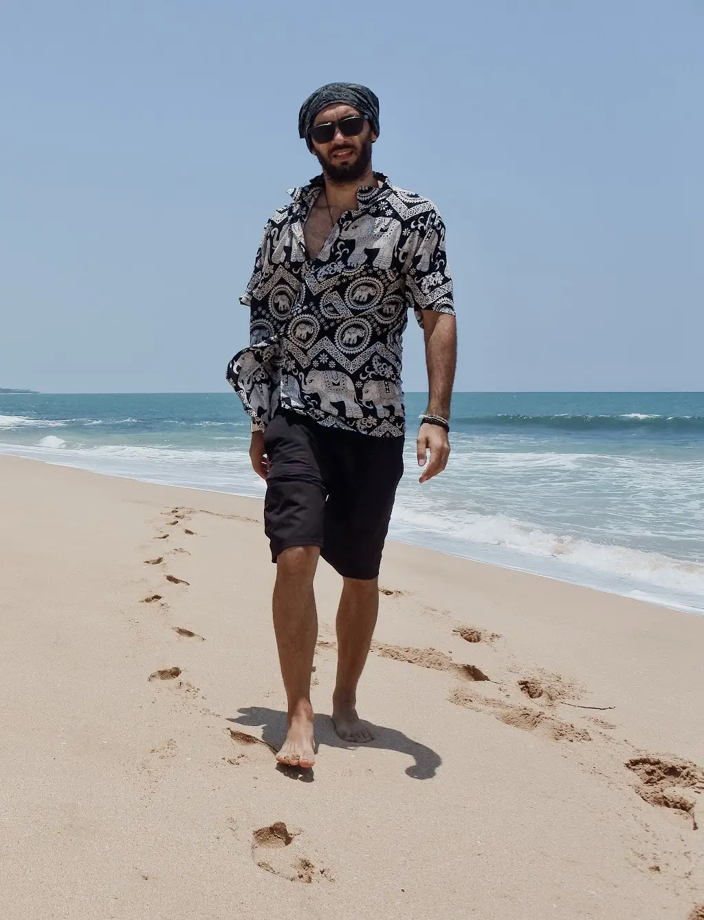 young travel photographer is walking on the beach with waves splashing behind him